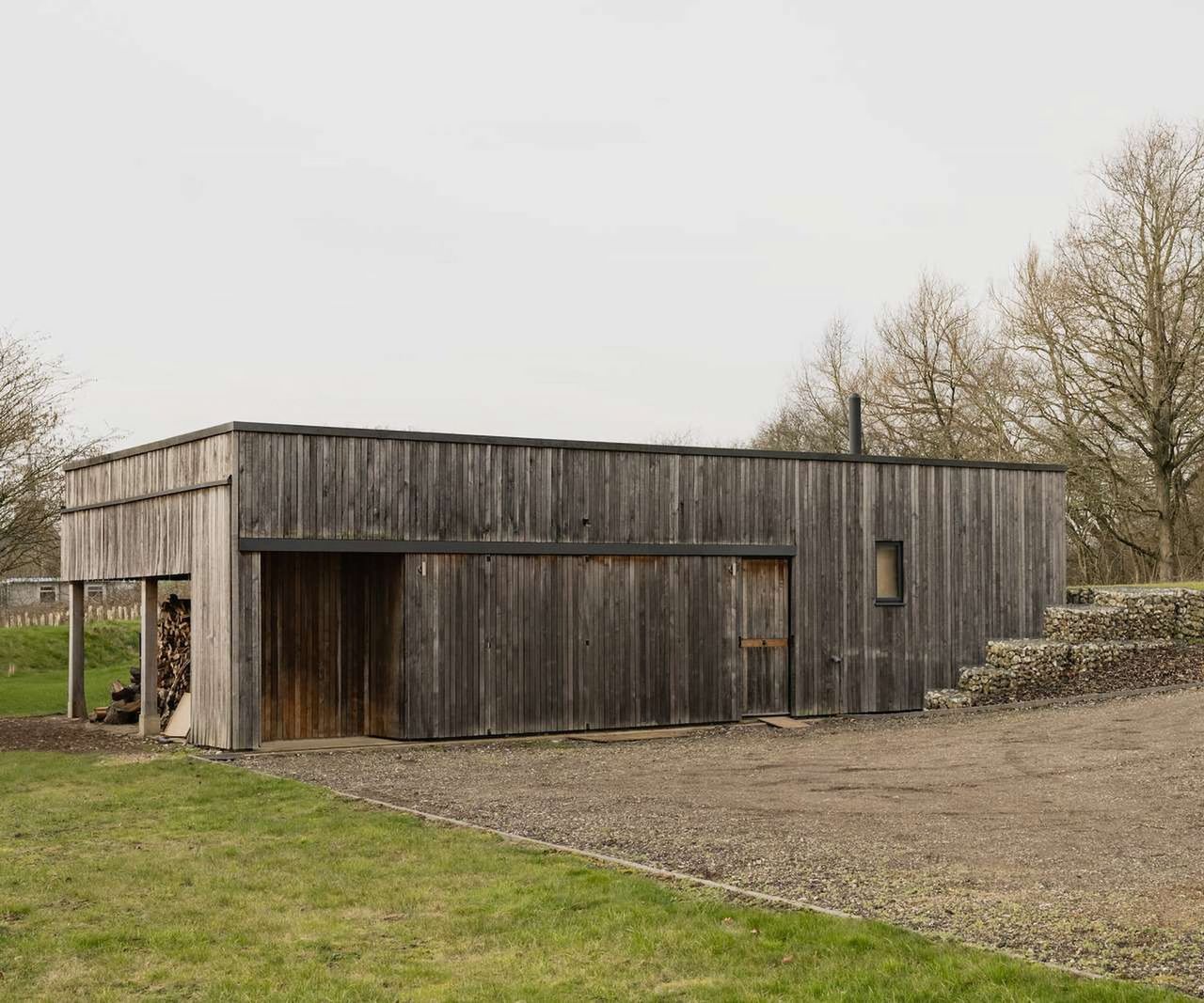 A timber clad outbuilding with a gabion wall