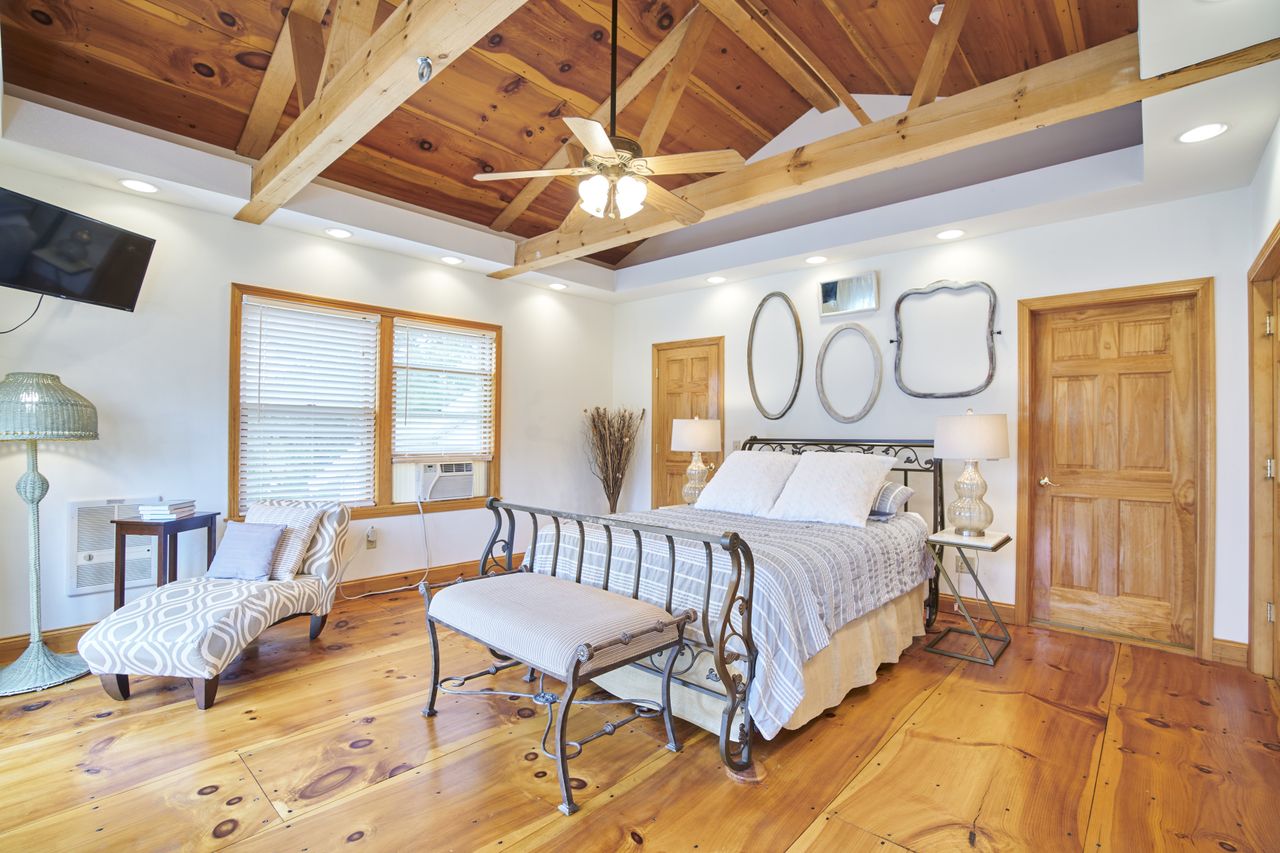 A bedroom with wooden floors and vaulted wooden ceiling with beams