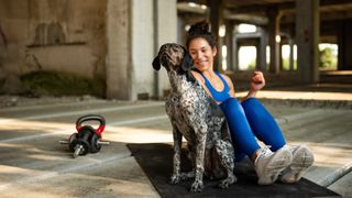 Woman sitting on an exercise mat with her dog during workout