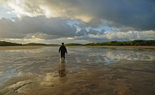 Ireland, County Mayo, Clew Bay, Rear view of man standing water in rubber boots, clouds in sky.