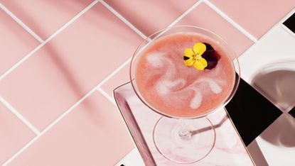 Still life image of a pink drink in a martini glass with edible flower garnish shot on tiled surface
