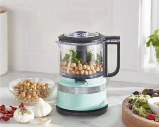 A mint green KitchenAid 3.5 Cup Food Chopper on a kitchen counter with bowls of food nearby