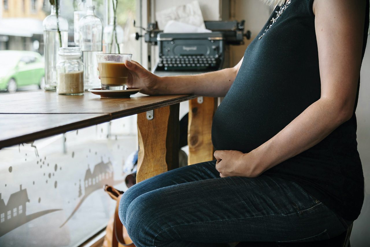 A pregnant women in a coffee shop with a coffee