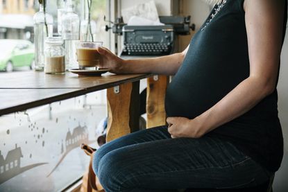 A pregnant women in a coffee shop with a coffee