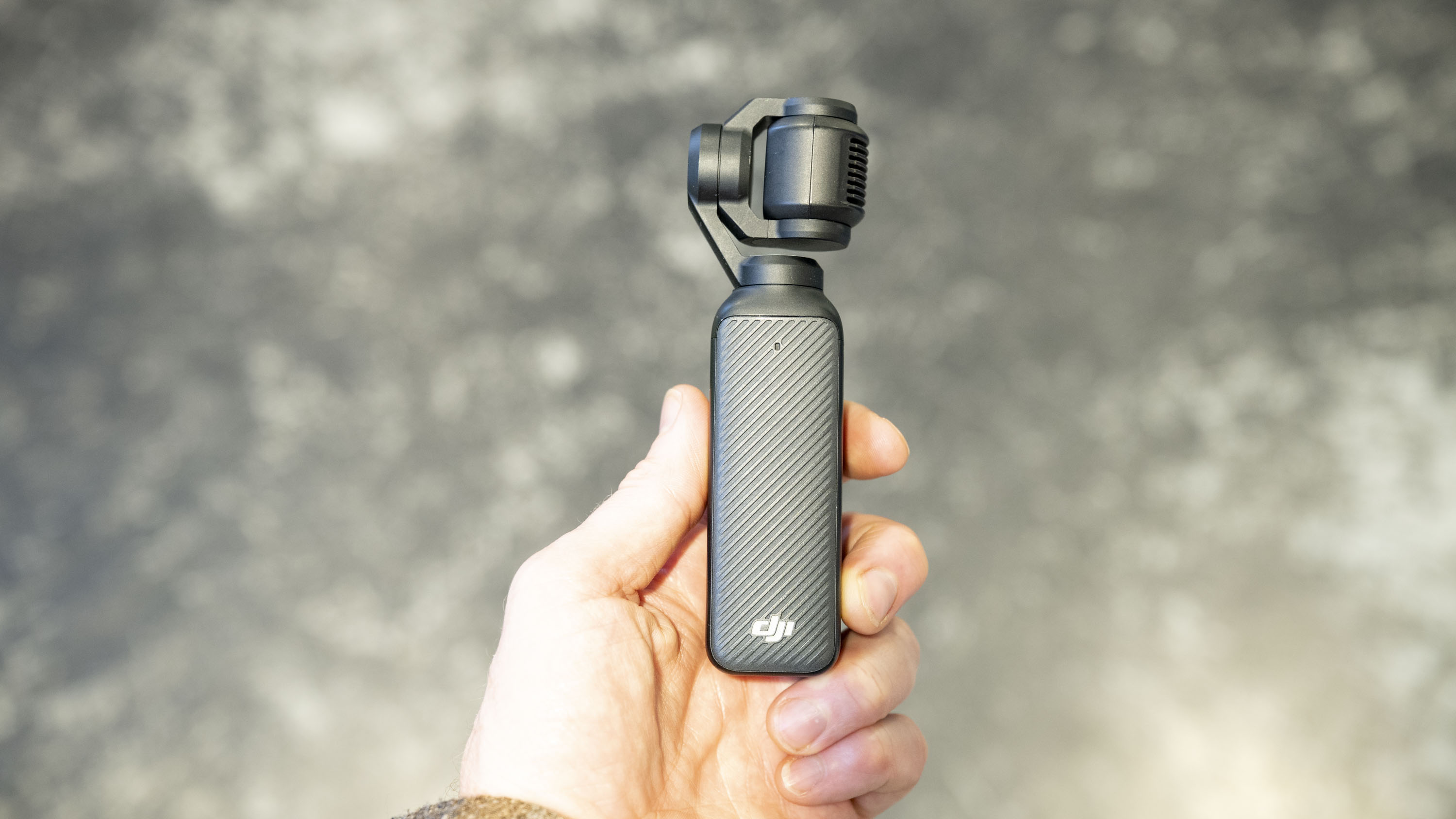 DJI Osmo Pocket 3 vlogging camera in user's hand, grey floor in background