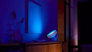 A Philips Hue Iris smart HomeKit lamp on a desk, with its blue light shining onto a wall.