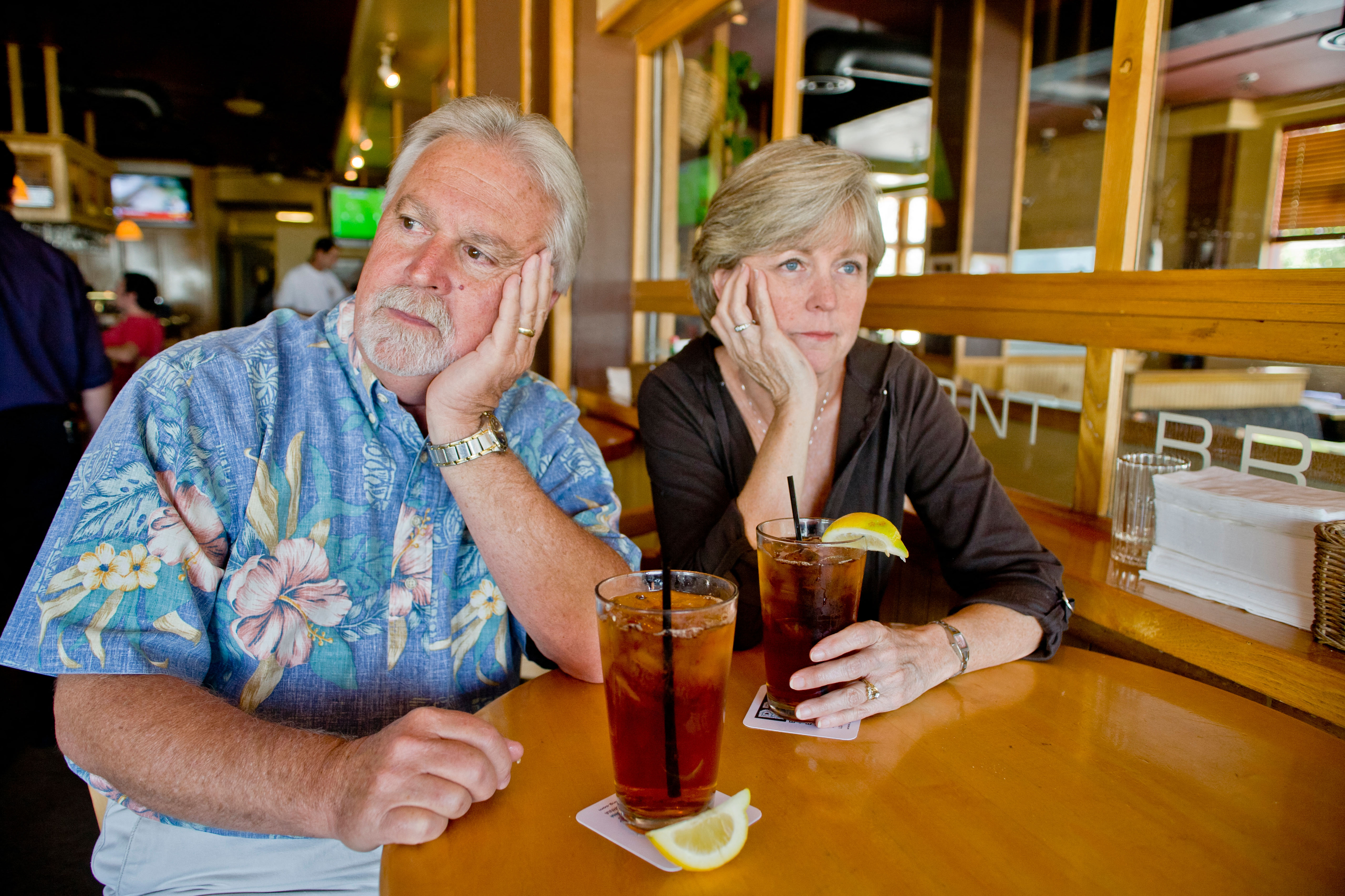 A middle aged couple appeared indifferent to each others' company over iced tea together in a restaurant