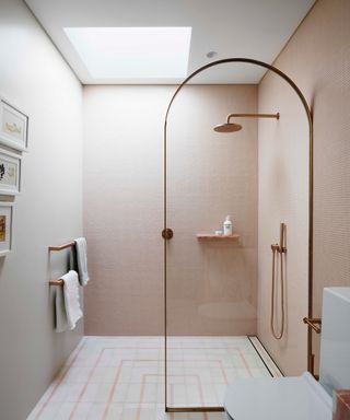 An ensuite walk-in shower with pink wall tiles and gold hardware