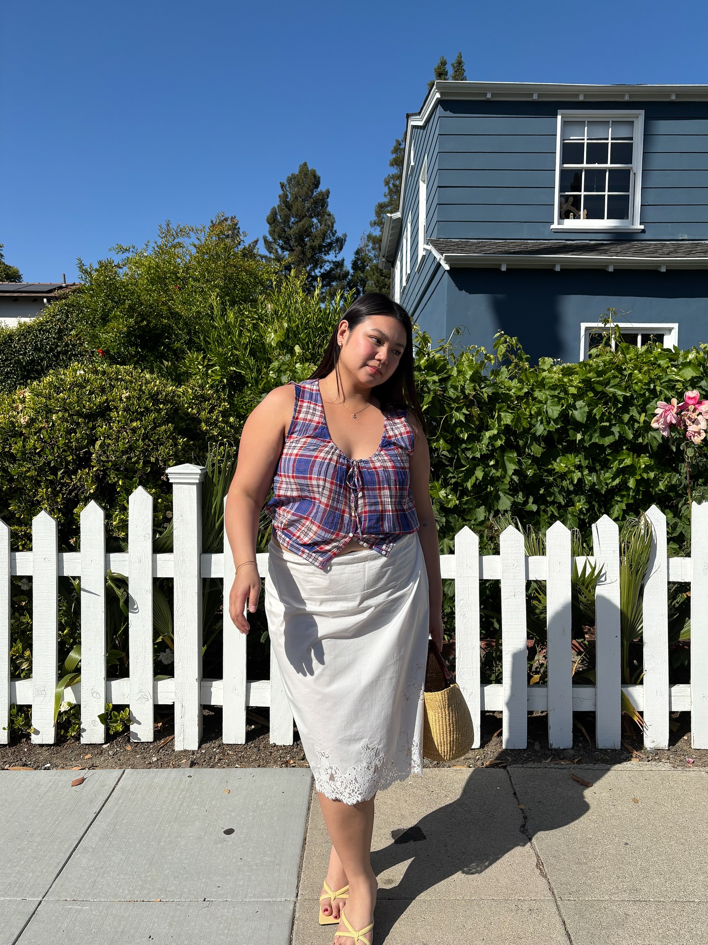 An image of @marina_torres wearing one of the best linen skirts from Doen with a plaid top and a raffia bag.