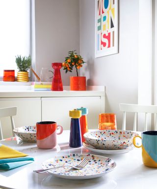 White dining table with orange cups and terrazzo plates
