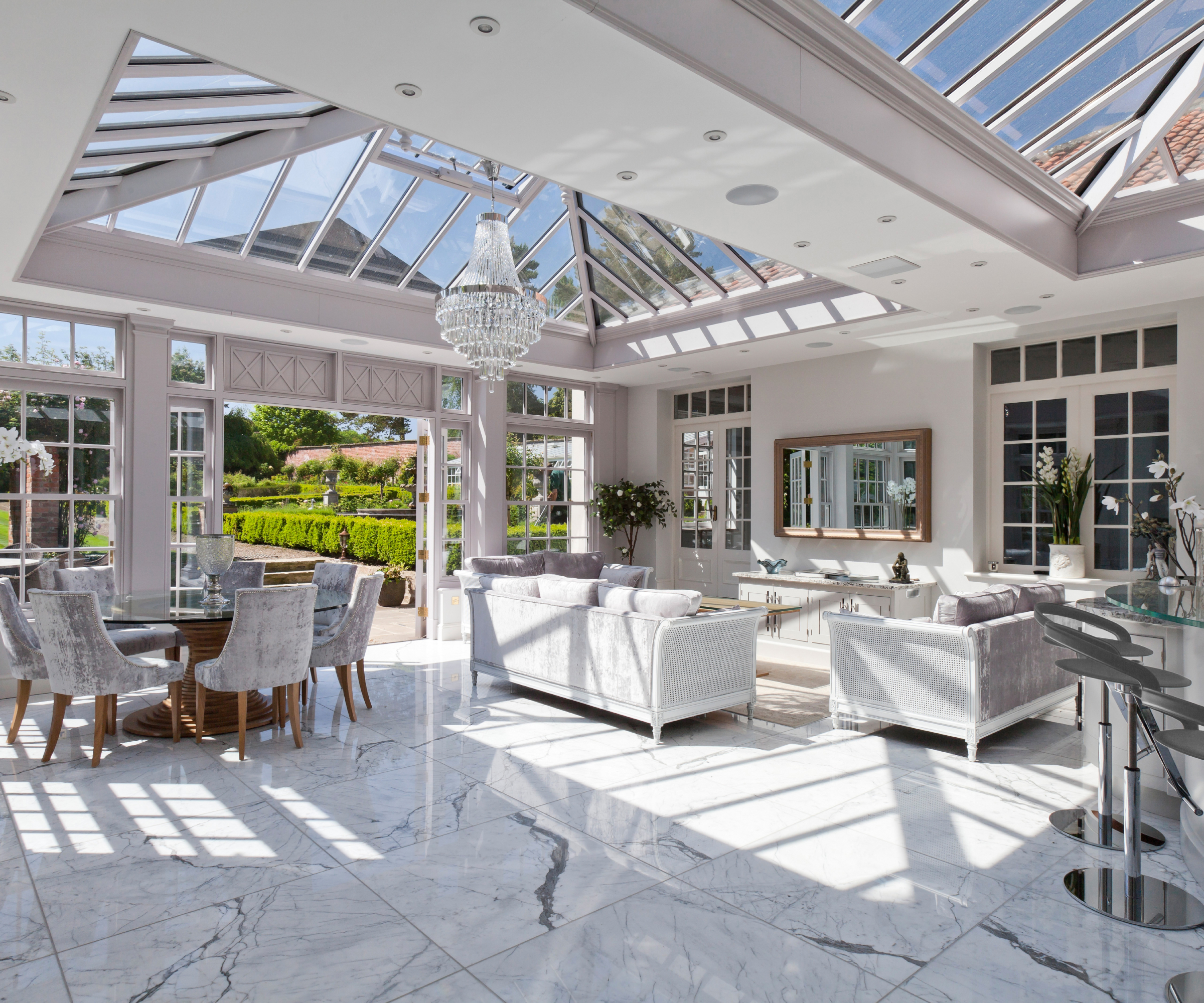 modern orangery interior with white marble floor, pale furniture, double rooflights, dining area, seating area and bar area to one corner