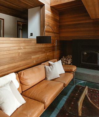 A camel colored leather sofa with white and beige cushions on top, against a wood paneled wall