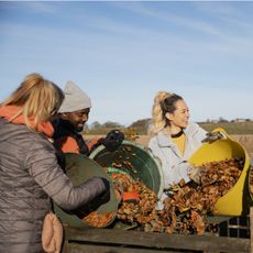 Smiling gardeners add autumn leaves to a compost bin