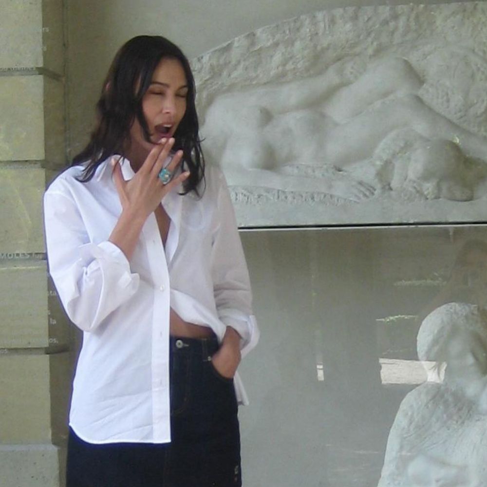 Alexa Chung wears a black denim miniskirt with silver bow heels and a white cotton button-down shirt.