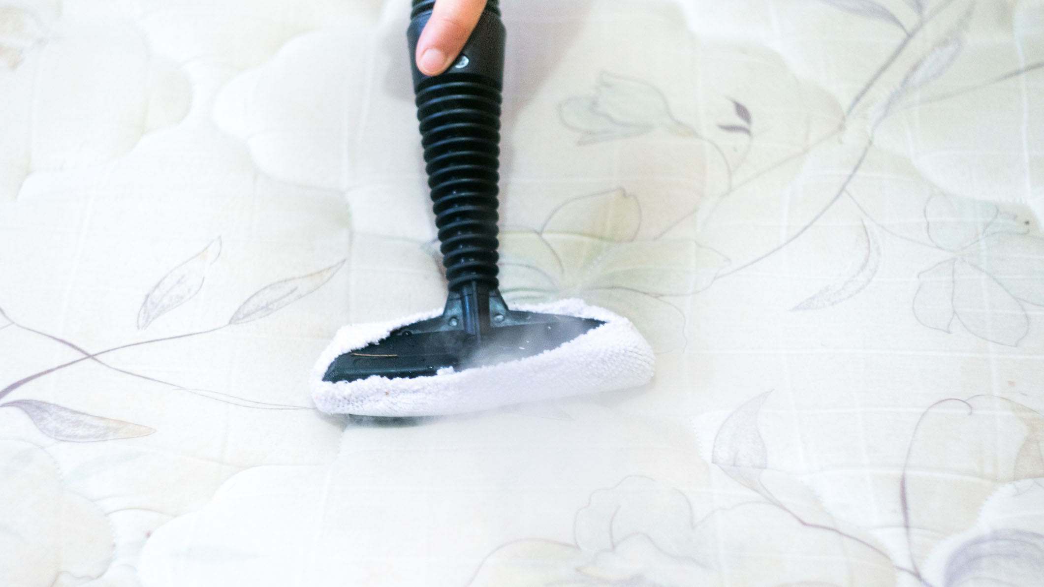 Person reinigt eine weiße Matratze mit Blumenmuster mit Dampf, um Bettwanzenreste zu entfernen