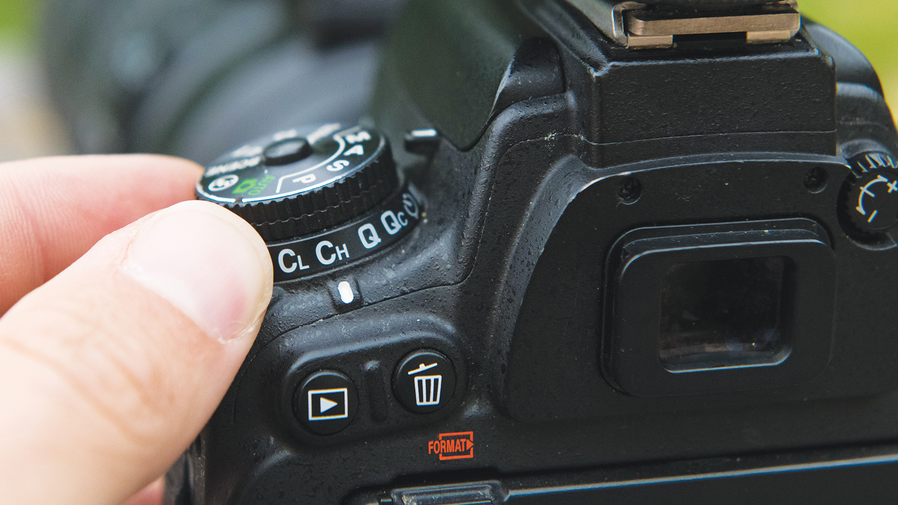 Close-up of a person&#039;s hand adjusting the dial on a DSLR camera, showcasing various settings and buttons on its rear