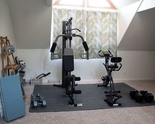 A home gym setup with gym equipment, mat and window covered with curtains