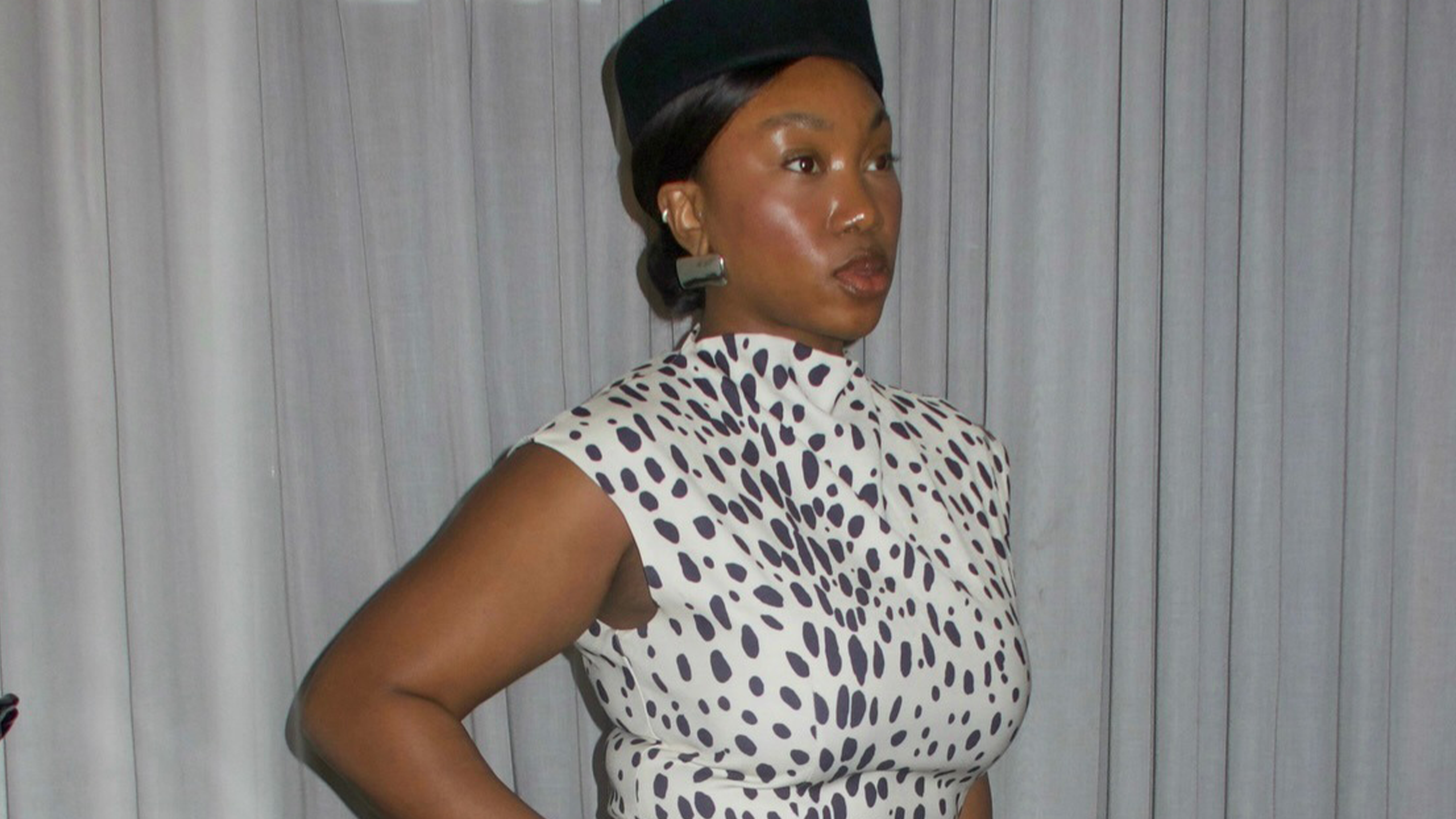 Woman wearing black and white dalmatian print dress and black pillbox hat.