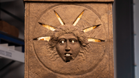 close-up of a stone altar with a humanlike face and rays making up a crown