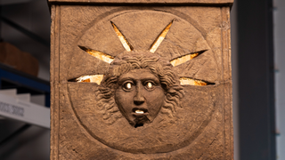 close-up of a stone altar with a humanlike face and rays making up a crown