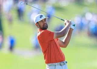 Tony Finau, wearing an orange polo and white cap, hits an iron shot