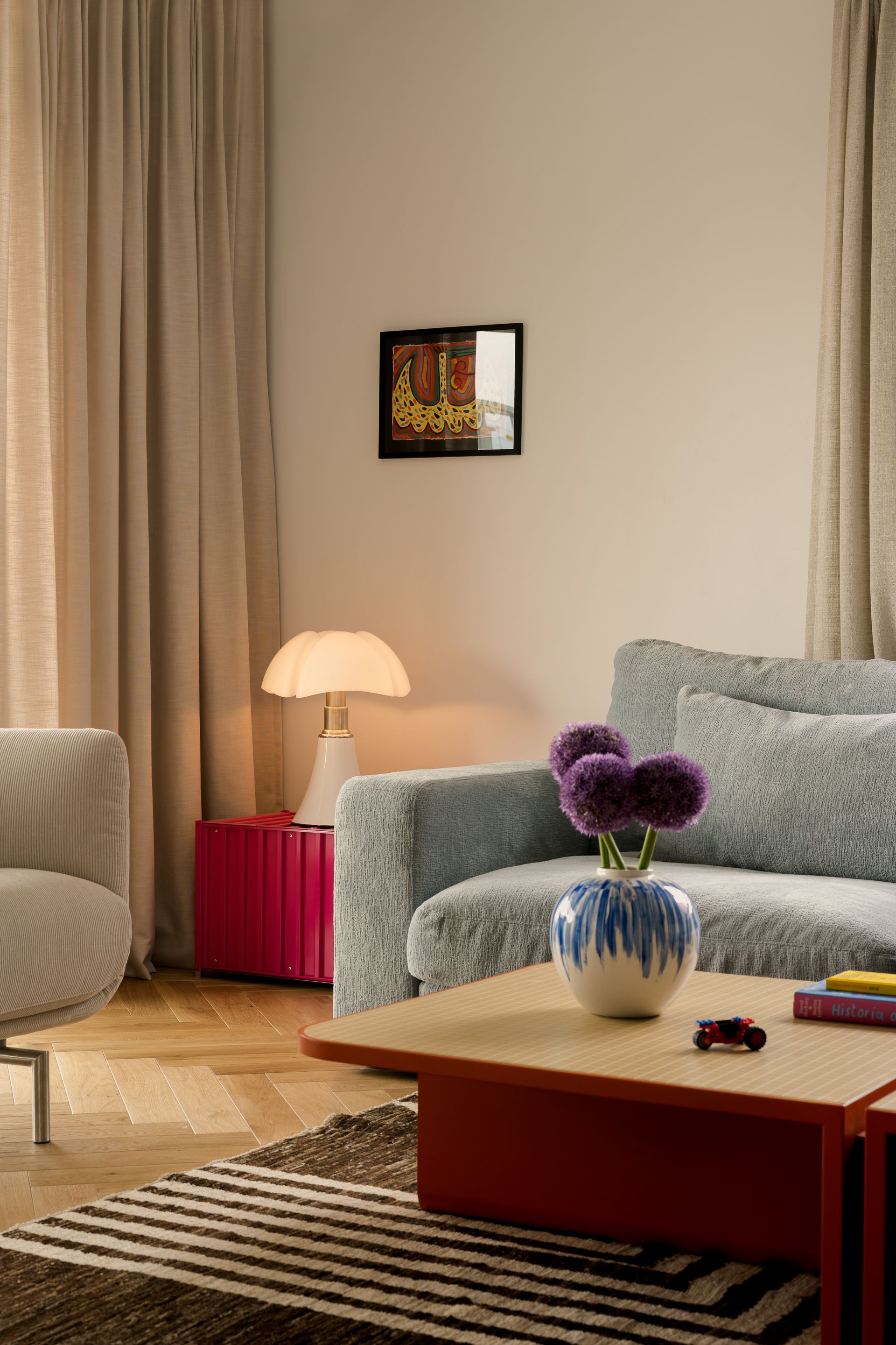A living room plays with calm and colour at once &ndash; red tables and neutral walls