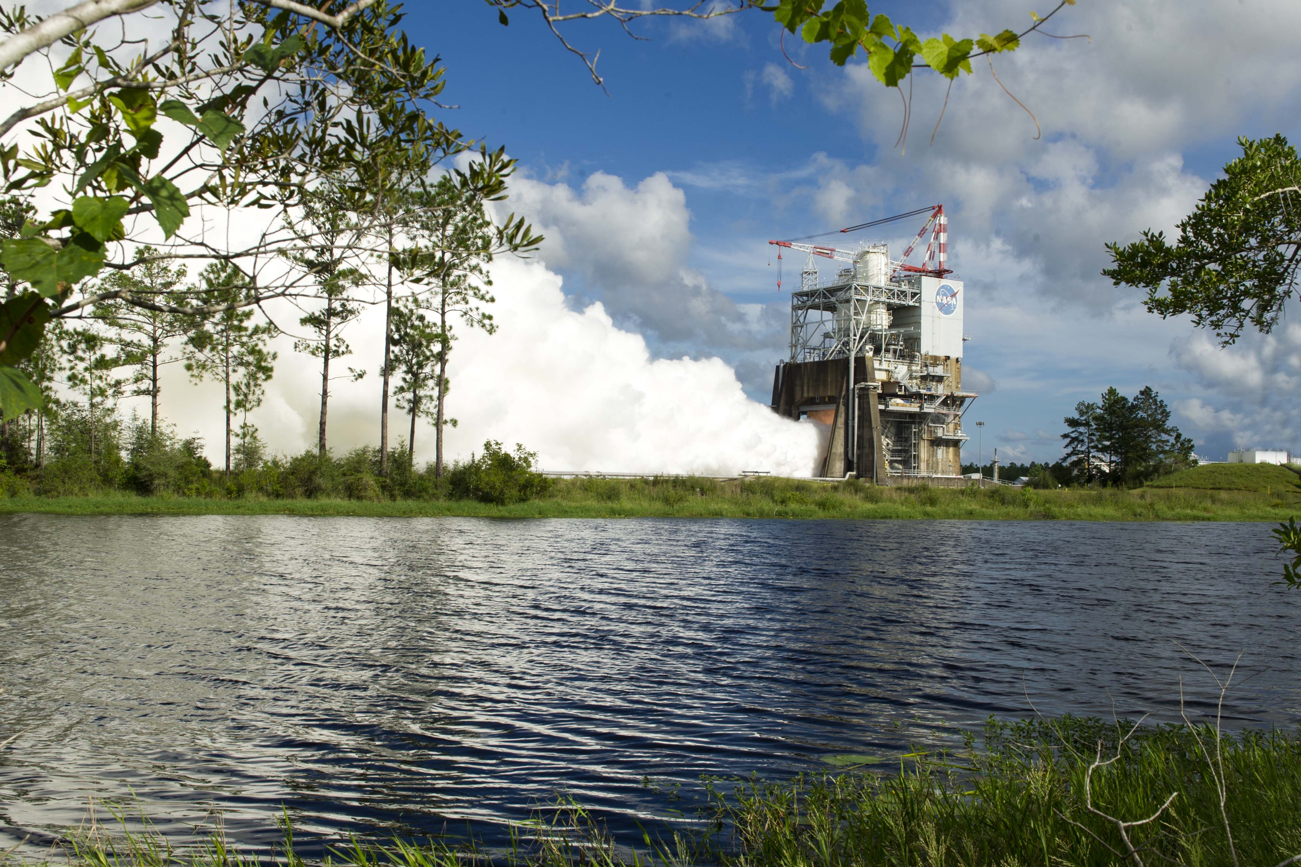 Steam billows out of a NASA structure with a body of water in the foreground