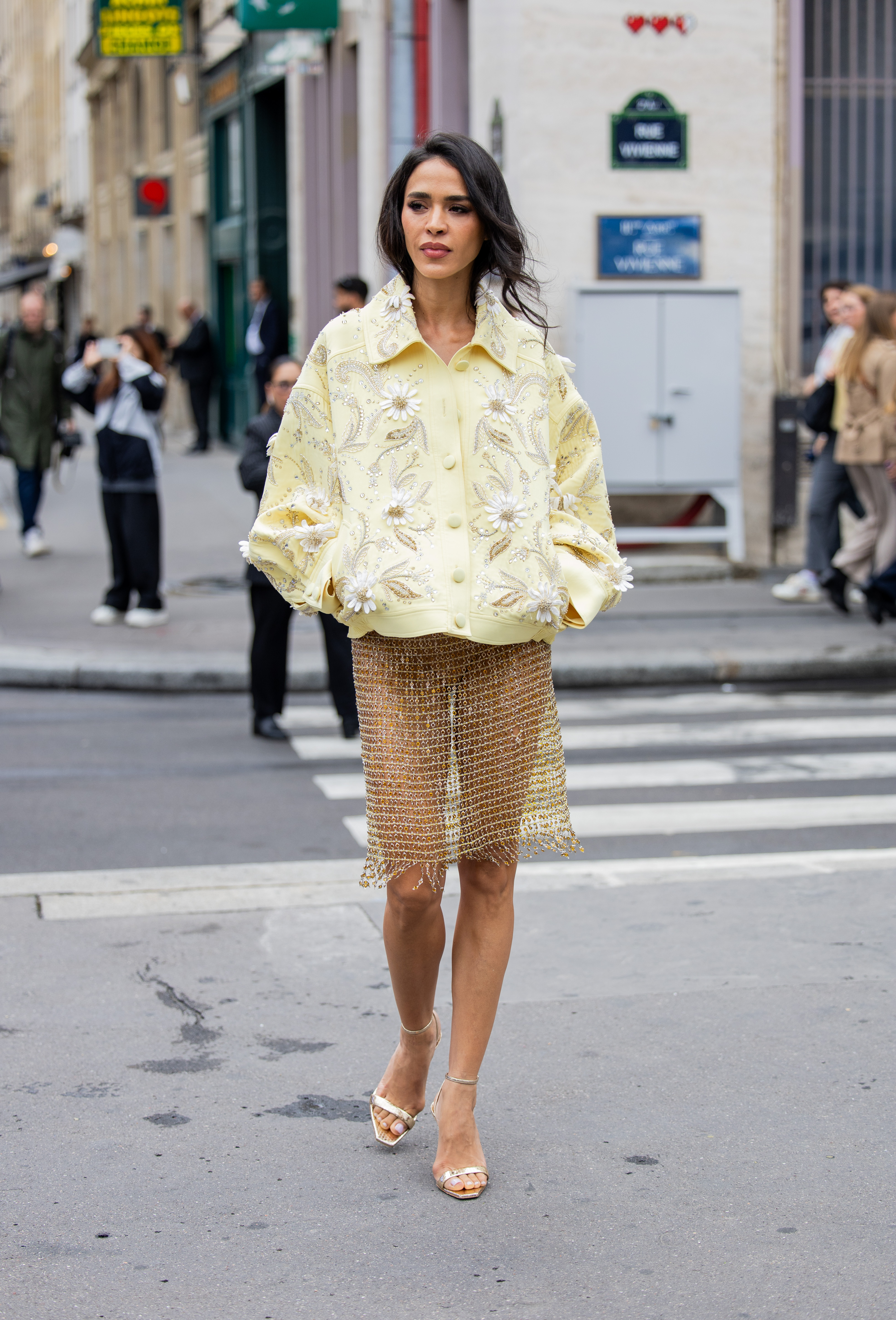 A Couture Fashion Week guest wears a yellow bomber jacket and mesh skirt with gold heeled sandals