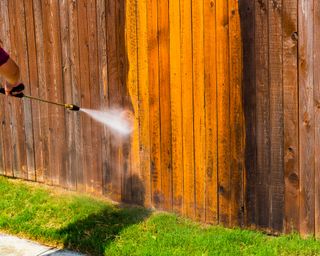 Cleaning a wooden fence with a pressure washer before staining