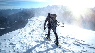 Best snowshoes - rear view of a caucasian climber on a snowy ridge under a snow storm
