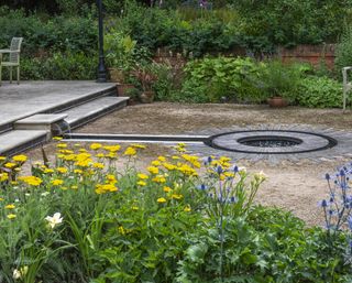 A short rill leads from the raised terrace to double circles of inky water with a central bubble fountain. The circular water feature is set into a sun style design created from laying slates on their sides