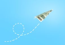 paper airplane made of US dollar flying against a sky background