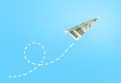 paper airplane made of US dollar flying against a sky background