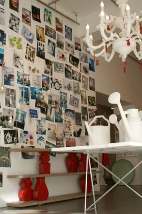 White watering cans and a white chandelier, in front of a wall of photographs
