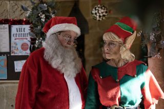 Jeremy (Robin Askwith), dressed as Santa, and Judith (Sue Holderness), dressed as an elf, have a conversation in a quiet corner of their grotto. Judith looks perturbed