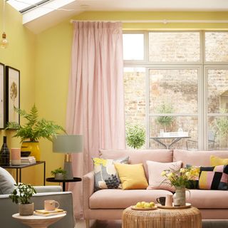 living room with yellow wall white window with pink curtain and pink sofa with designed cushions