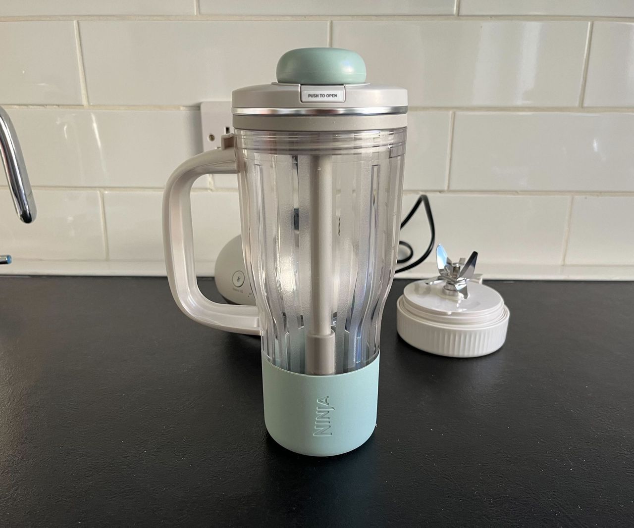 A clear plastic tumbler cup with a blue base and large grey handle.