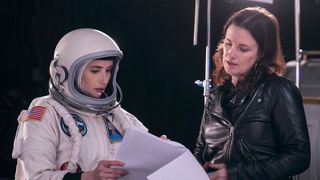 an actress in a spacesuit talks to a woman in a black leather jacket on a movie set