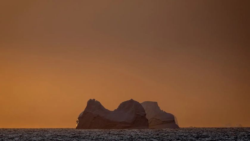 a view of a glacier in the ocean with an orange sky behind it