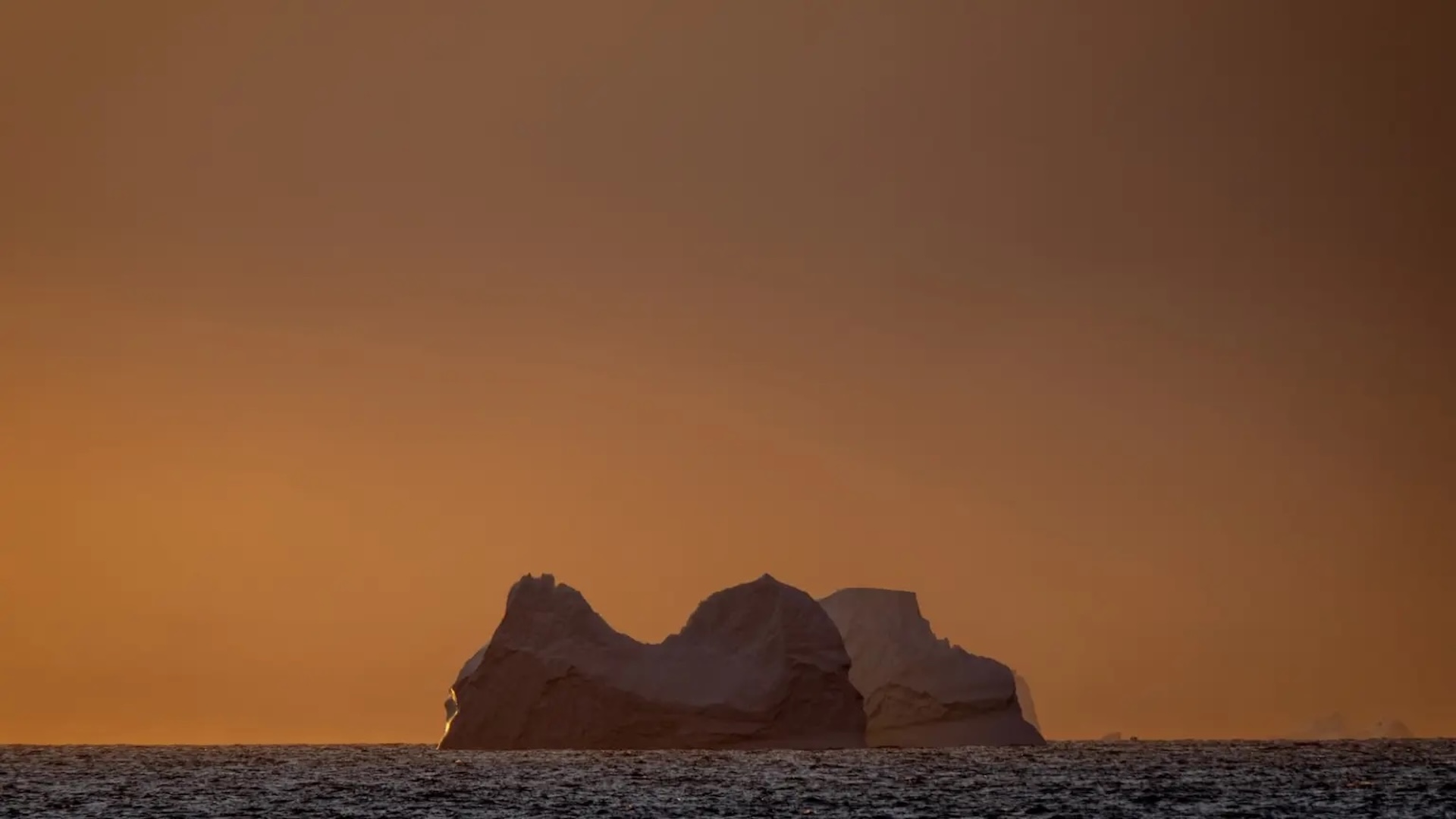 a view of a glacier in the ocean with an orange sky behind it