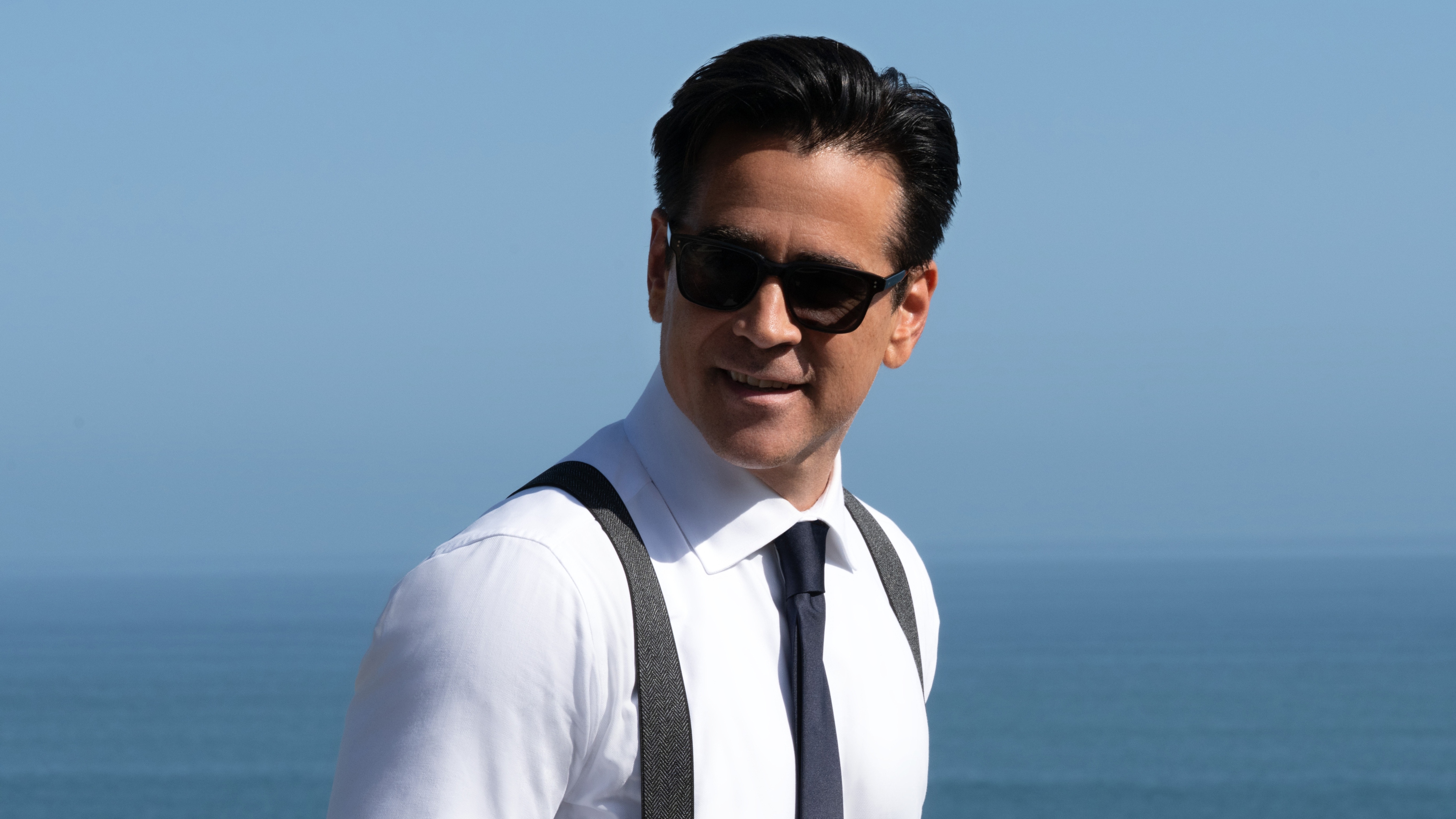 Colin Farrell as John Sugar smiling and wearing sunglasses with a white shirt, black tie and braces.