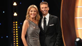 Vanna White and Ryan Seacrest standing next to each other and smiling on Celebrity Wheel of Fortune.