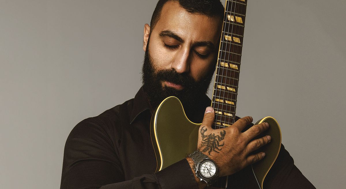 Aryan King cradles his Gibson ES-335 in matte drab Olive Green. He has a scorpion tattoo on his hand.