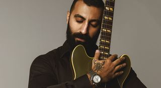 Aryan King cradles his Gibson ES-335 in matte drab Olive Green. He has a scorpion tattoo on his hand.