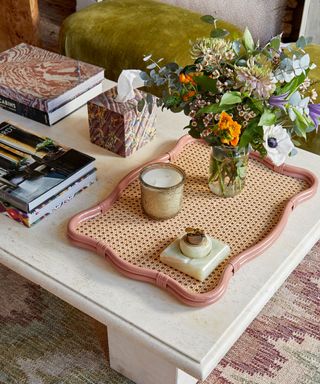 marble coffee table with pink wavy tray with fresh flowers and candles and stacks of books