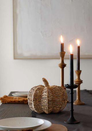 woven pumpkin and three neutral colored candle sticks on a set table