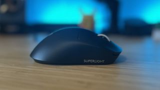 Side view of Logitech G Pro X Superlight 2 DEX gaming mouse on a wooden desk, showing mouse right flank with Superlight logo