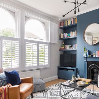 blue living room with cafe style shutters on windows, black Victorian fireplace and in built shelves in recesses