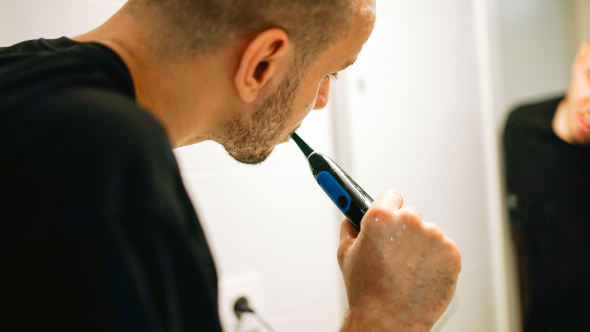 Image shows man brushing his teeth in mirror