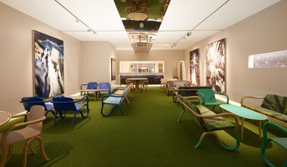View of the Netjets VIP lounge at Art Basel featuring light coloured wall panels, green flooring, wall art, chairs and oval shaped tables in different colours and a strip of mirror on the ceiling